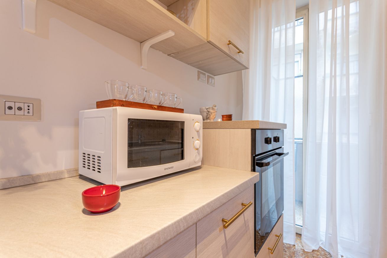 Une cuisine avec un micro-ondes blanc, un four et un saladier rouge posé sur le plan de travail.