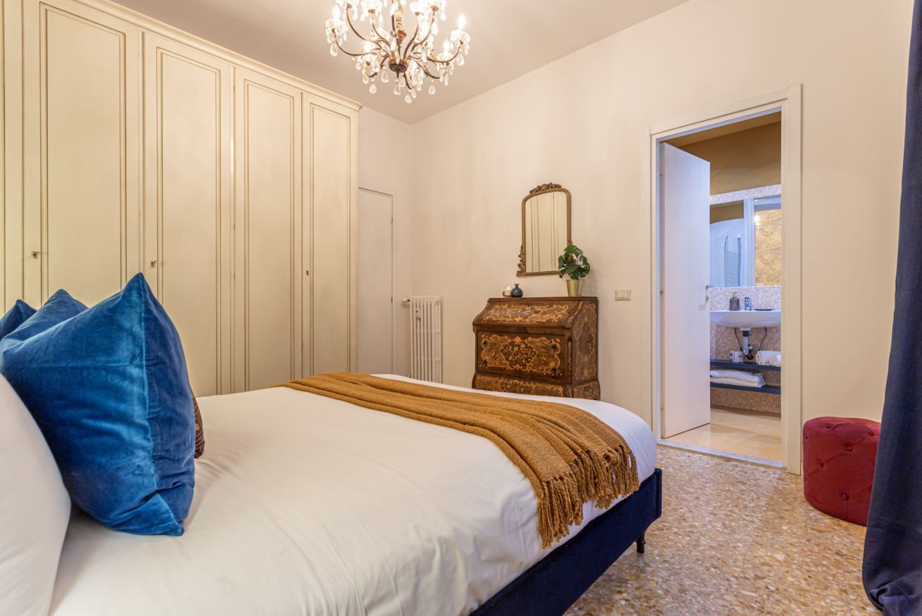 A bedroom with a large bed, a dresser, a mirror, and a chandelier.