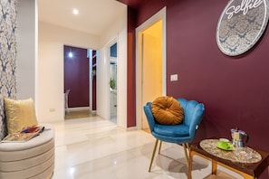 Ein modernes Wohnzimmer mit blauem Sessel, rundem Couchtisch und einer Couch mit gemustertem Kissen.