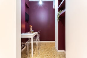 Un coin repas avec une table et des chaises blanches, une bougie sur la table et un mur d’un rouge foncé.