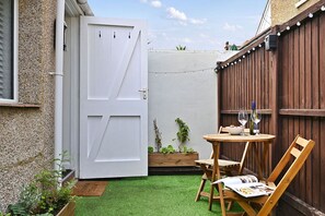 Een terras met een witte deur, een houten schutting en een kleine tafel met stoelen.
