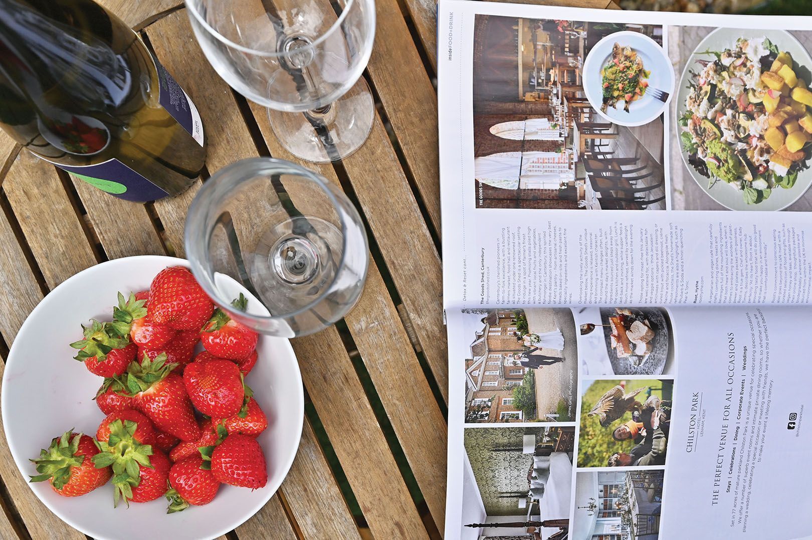 Une table avec un bol de fraises, une bouteille de vin et un verre à vin.