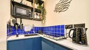 A kitchen with blue cabinets, a microwave, a kettle, and a sink with a water filter. - Stone's Throw - a holiday let that sleeps 2 guests in 1 bedroom (Hythe)