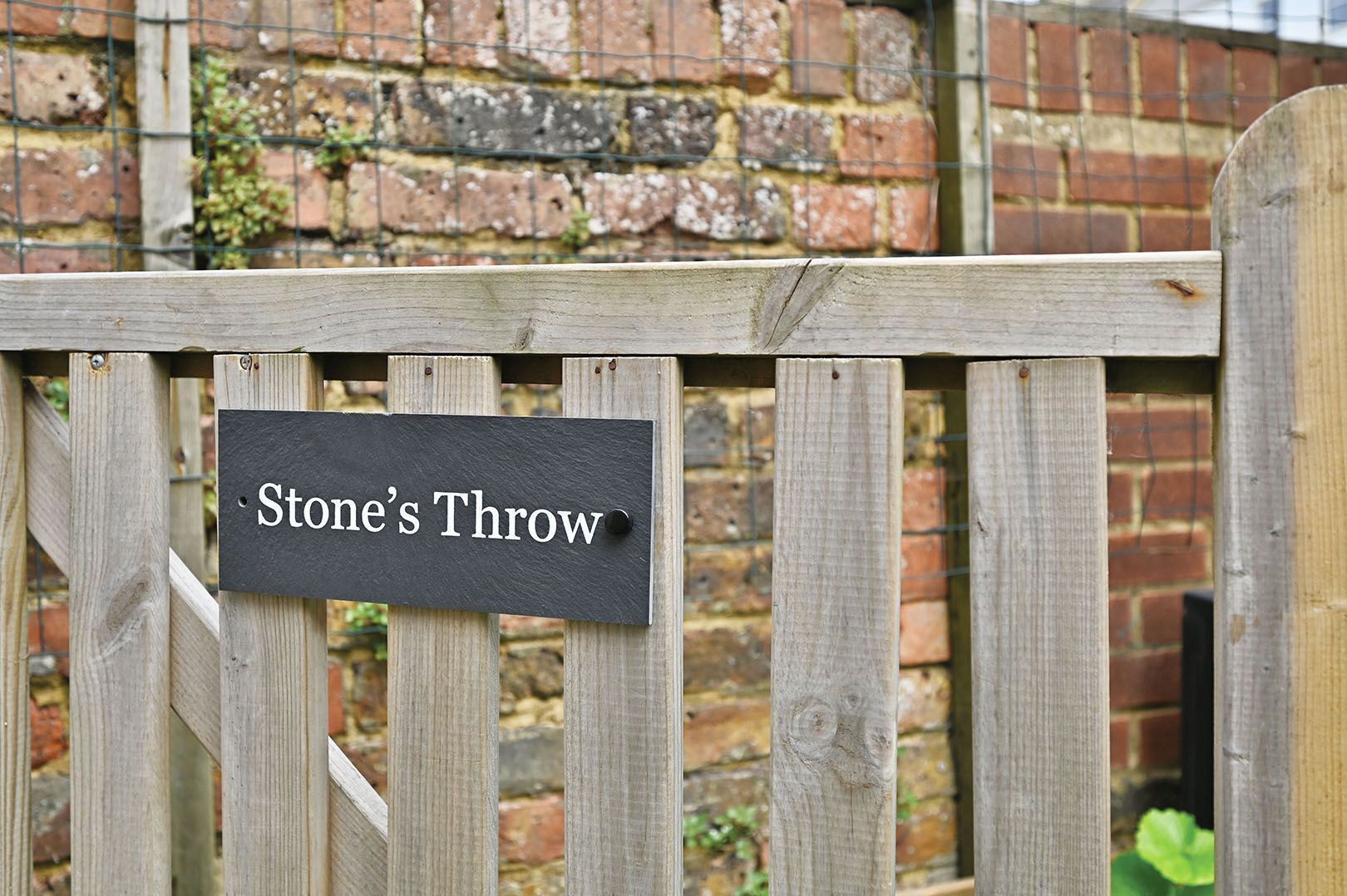 Un cancello di legno con un cartello che recita 'Stone's Throw'.