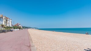 A pebbled beach with a paved walkway, buildings on one side, and the sea in the background. - Stone's Throw - a holiday let that sleeps 2 guests in 1 bedroom (Hythe)