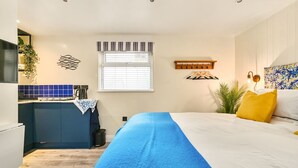 A modern bedroom with a bed, a small kitchenette, and a window with blinds. - Stone's Throw - a holiday let that sleeps 2 guests in 1 bedroom (Hythe)
