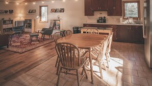 A spacious kitchen with wooden cabinets, a dining table, and chairs. There are bookshelves, a coffee machine, and a refrigerator. - Boreal Retreat  |  Cabin in the Pines | Port Wing (Port Wing)