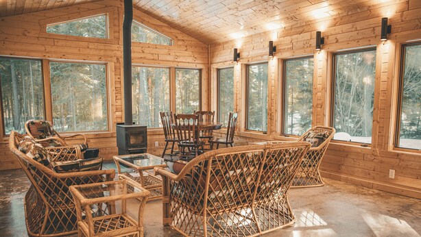A log cabin interior with large windows, a fireplace, wicker furniture, and a polished concrete floor. - Boreal Retreat  |  Cabin in the Pines | Port Wing (Port Wing)