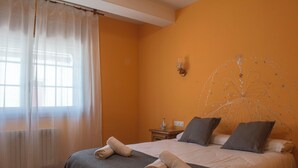 Een hotelkamer met een bed, nachtkastje, een wandlamp en een raam met dunne gordijnen.