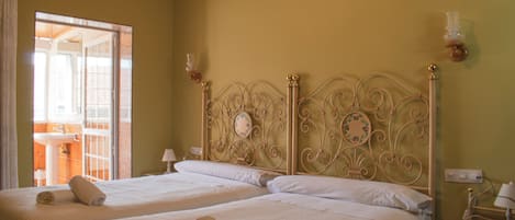 Habitación de hotel con dos camas, un baño visible a través de una puerta abierta y una mesita de noche con lámpara.