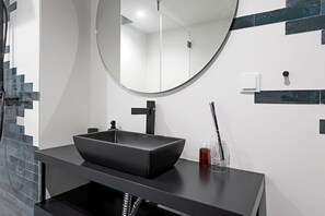 Ein modernes Badezimmer mit einem schwarzen Vessel-Waschbecken, einem runden Spiegel und einer schwarzen Arbeitsplatte.