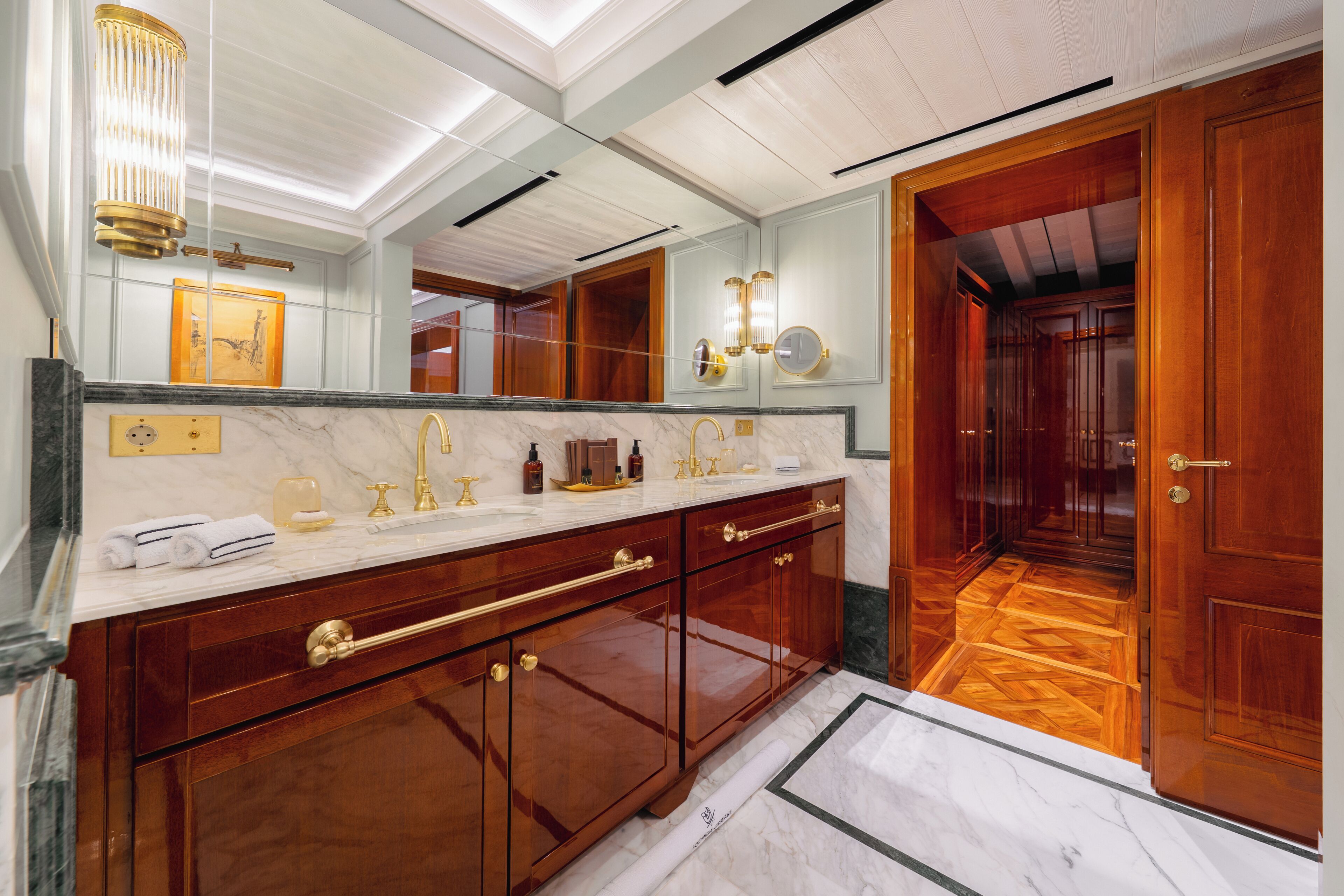 A luxurious bathroom with a large mirror, marble countertop, and wooden cabinetry.