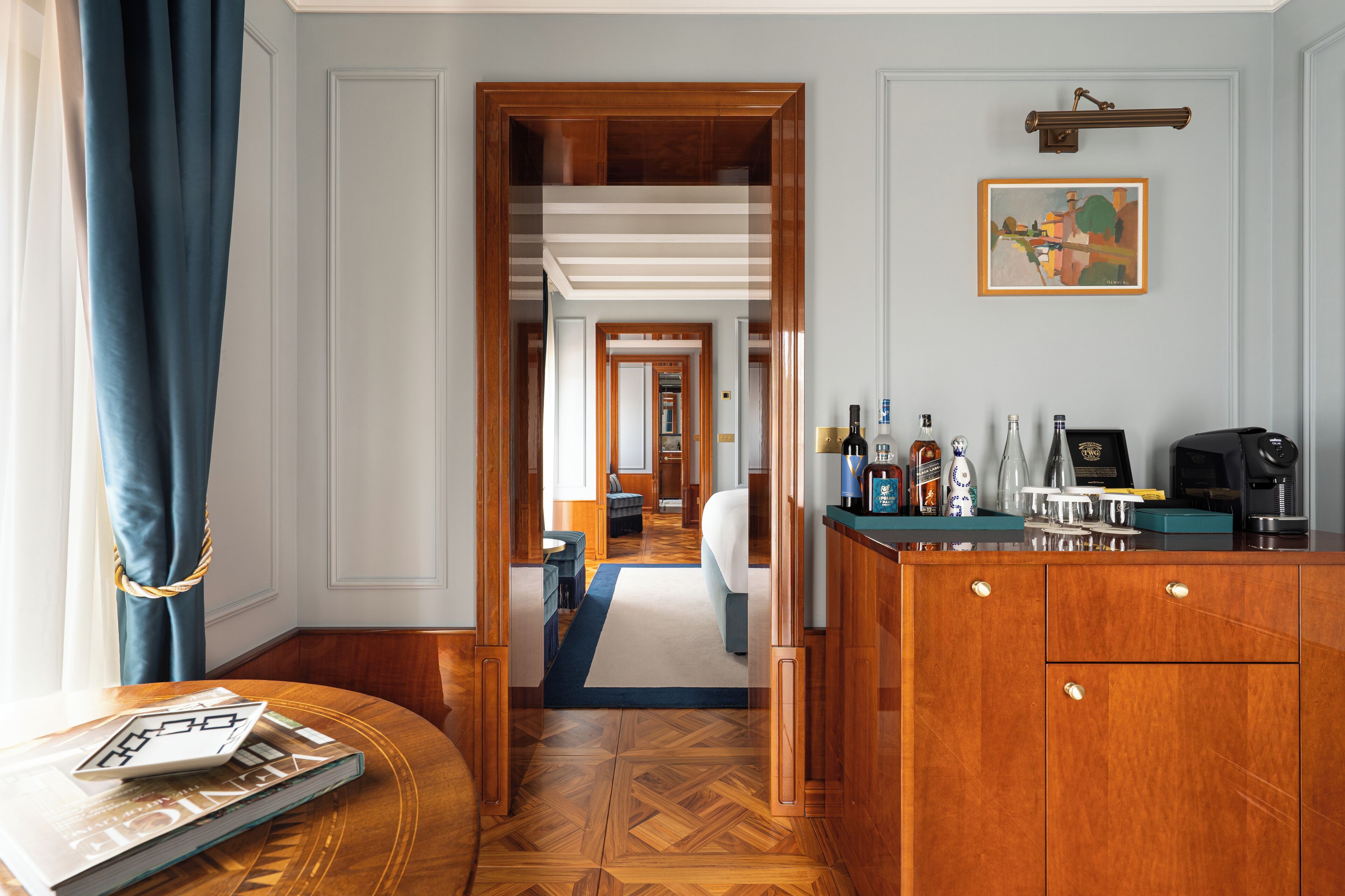 Habitación de hotel con piso de madera, zona de bar con botellas y vasos, y vista al pasillo.