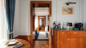 Habitación de hotel con piso de madera, zona de bar con botellas y vasos, y vista al pasillo.