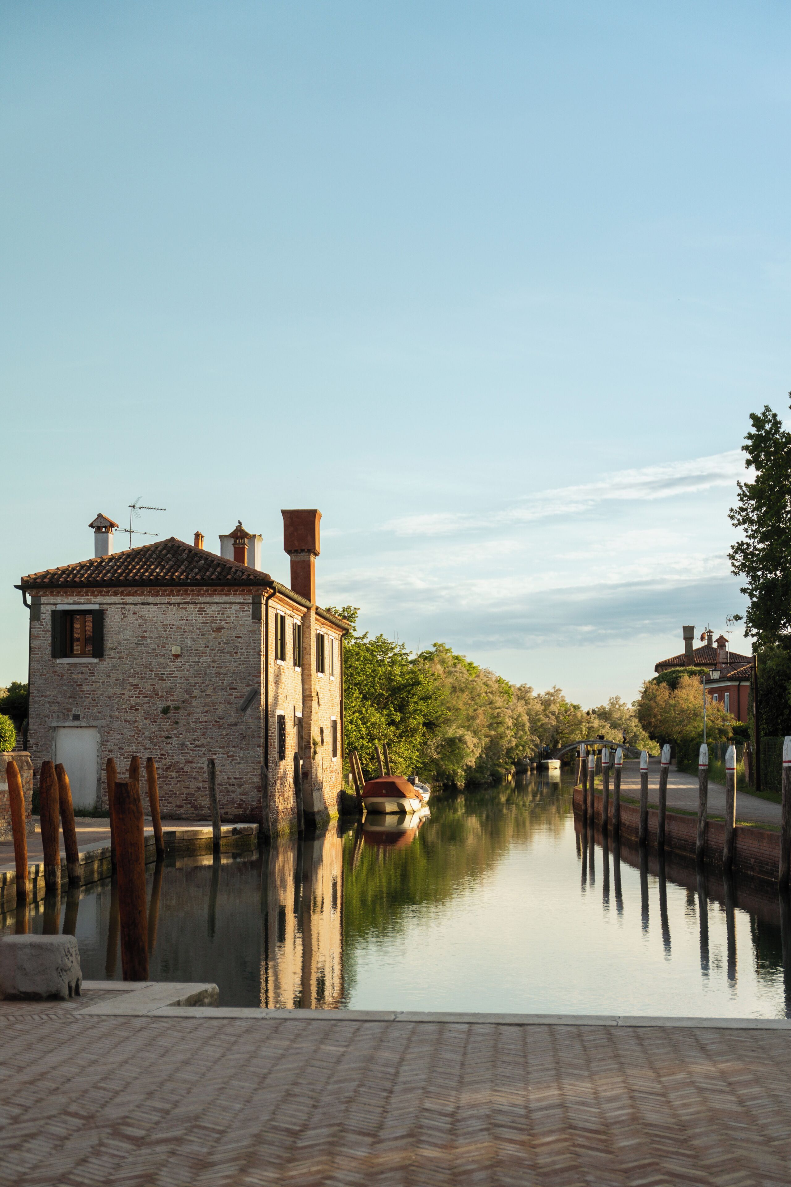 A canal with a brick building, a boat, and a bridge.