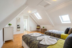 Ein helles, modernes Schlafzimmer im Dachgeschoss mit zwei Betten, einem kleinen Schreibtisch und einem Spiegel.