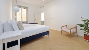 Un dormitorio con cama, mesita de noche, silla y una planta en maceta.