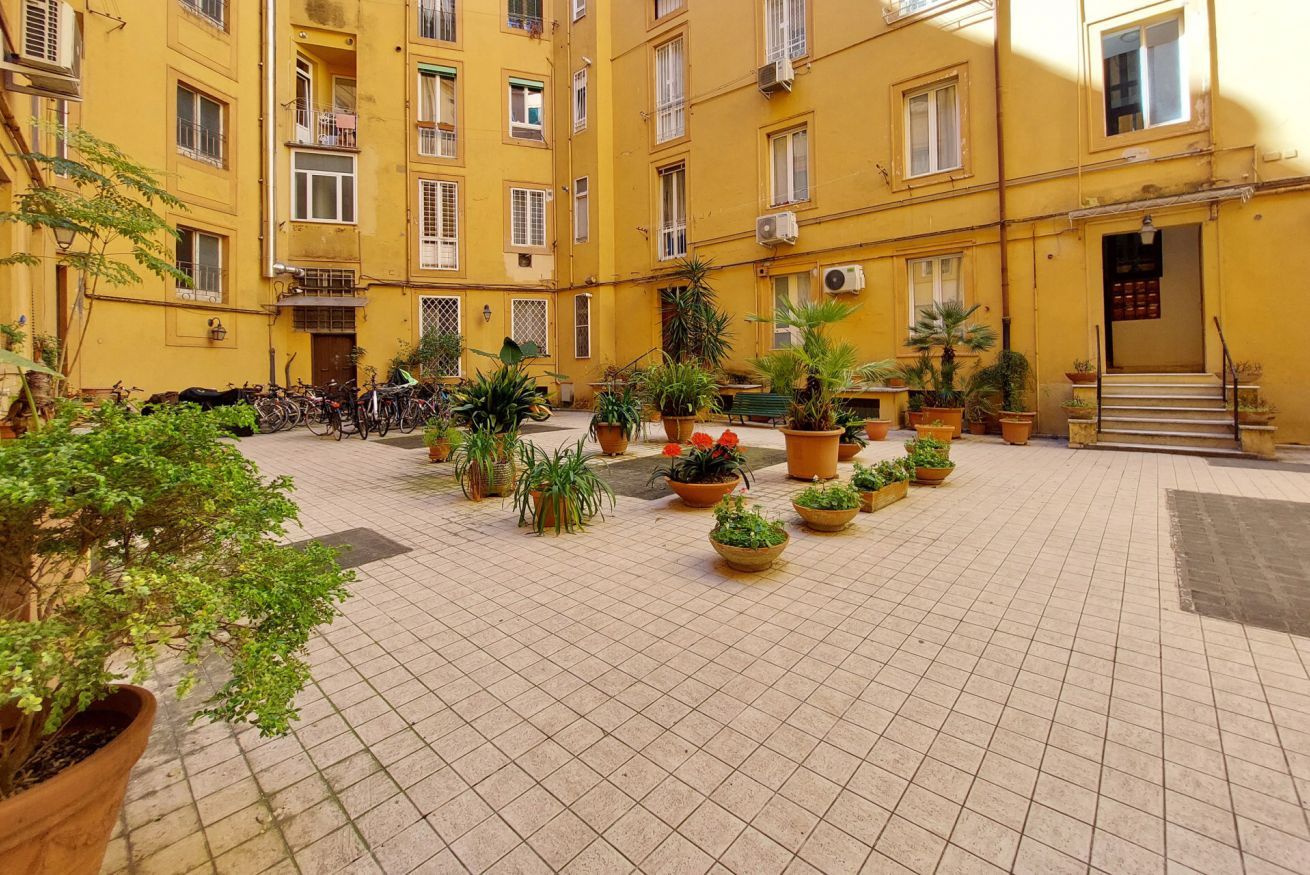 A courtyard with tiled flooring, yellow buildings, and potted plants.