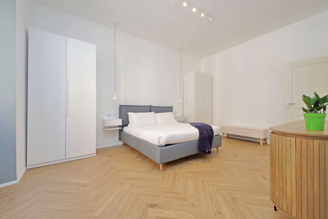 Un dormitorio moderno con cama, armario, mesita de noche, banco y una pequeña planta verde.