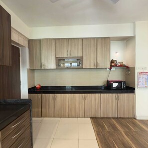 A modern kitchen with wooden cabinets, a black countertop, and a microwave. - LONAVALA TURGARLI-ESCAPE TO BYGONE ERAA HOME WITH SOUL (Lonavala)