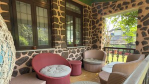 A covered outdoor seating area with wicker furniture, stone walls, and large windows. - LONAVALA TURGARLI-ESCAPE TO BYGONE ERAA HOME WITH SOUL (Lonavala)