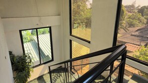 A staircase with a glass railing leading to a balcony with large windows overlooking a garden and buildings. - LONAVALA TURGARLI-ESCAPE TO BYGONE ERAA HOME WITH SOUL (Lonavala)