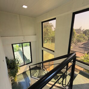 A staircase with a glass railing leading to a balcony with large windows overlooking a garden and buildings. - LONAVALA TURGARLI-ESCAPE TO BYGONE ERAA HOME WITH SOUL (Lonavala)