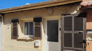A building with a beige facade, a white door, and two windows with shutters.
