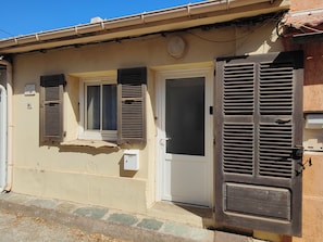 A building with a beige facade, a white door, and two windows with shutters. - A Casa Sulana—300 meters from the port of Macinaggio (Tomino)