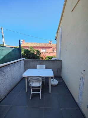 A small outdoor balcony with a white table and chairs, a concrete wall, and a view of buildings in the background. - A Casa Sulana—300 meters from the port of Macinaggio (Tomino)