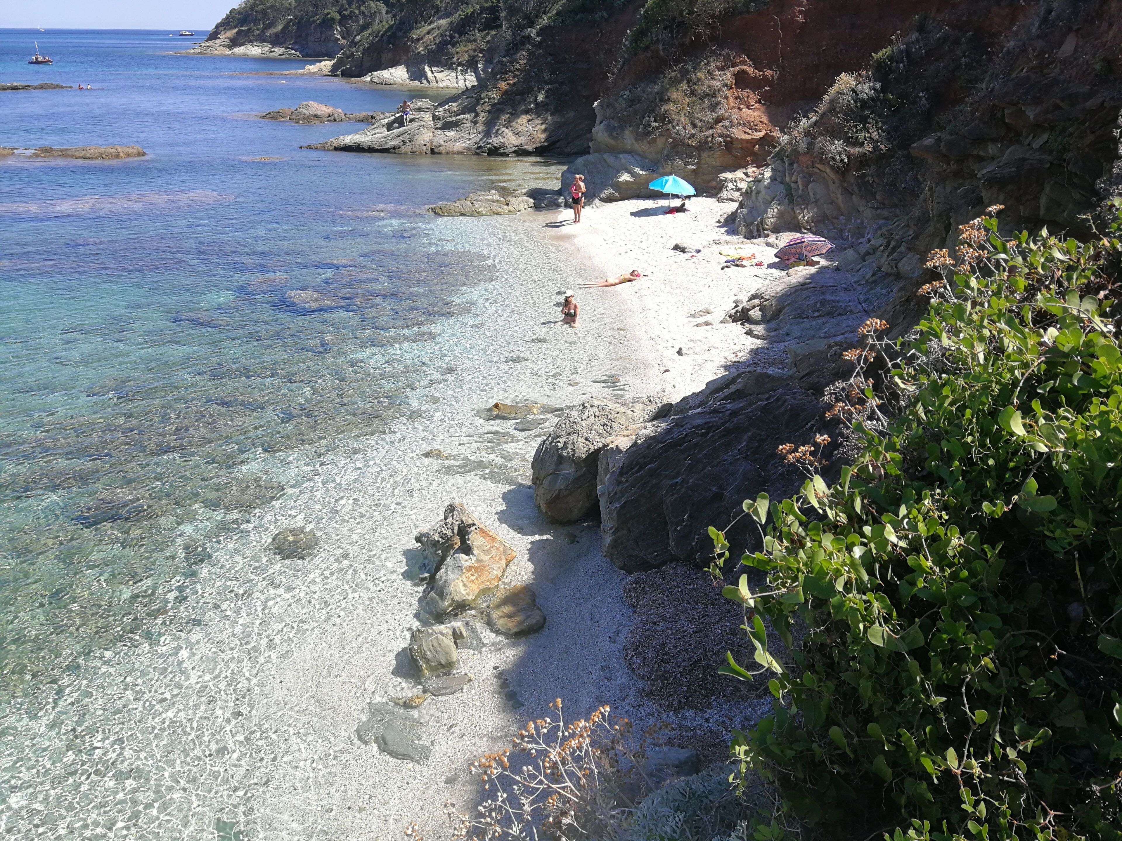 A coastal beach with clear water, rocky outcrops, and a few people.