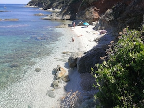 Een kuststrand met helder water, rotsformaties en enkele mensen.