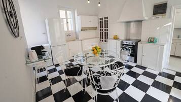 A kitchen with a checkered floor, white cabinets, a glass table with chairs, and a chandelier.