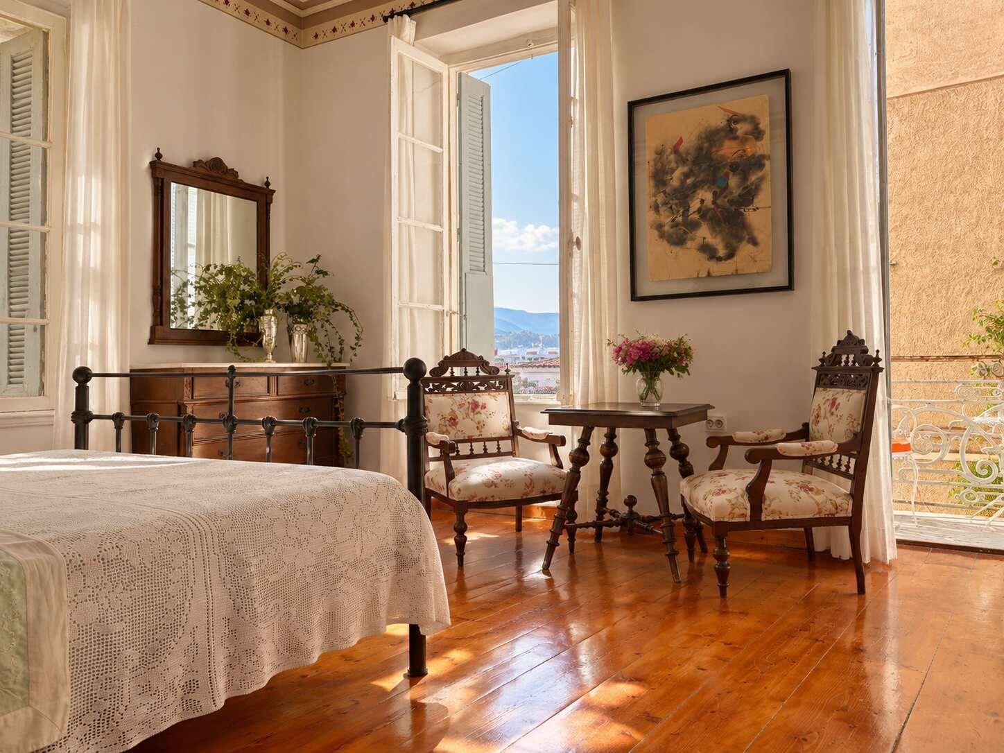 Un dormitorio con cama, dos sillas, una mesa, un espejo y un cuadro.