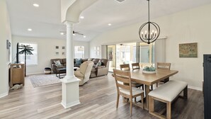 Uma sala de estar espaçosa com uma grande mesa de jantar de madeira, assentos confortáveis e um lustre moderno.