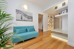 Ein modernes Wohnzimmer mit einem blauen Sofa, Holzboden und einer Wandregal mit Dekoration.