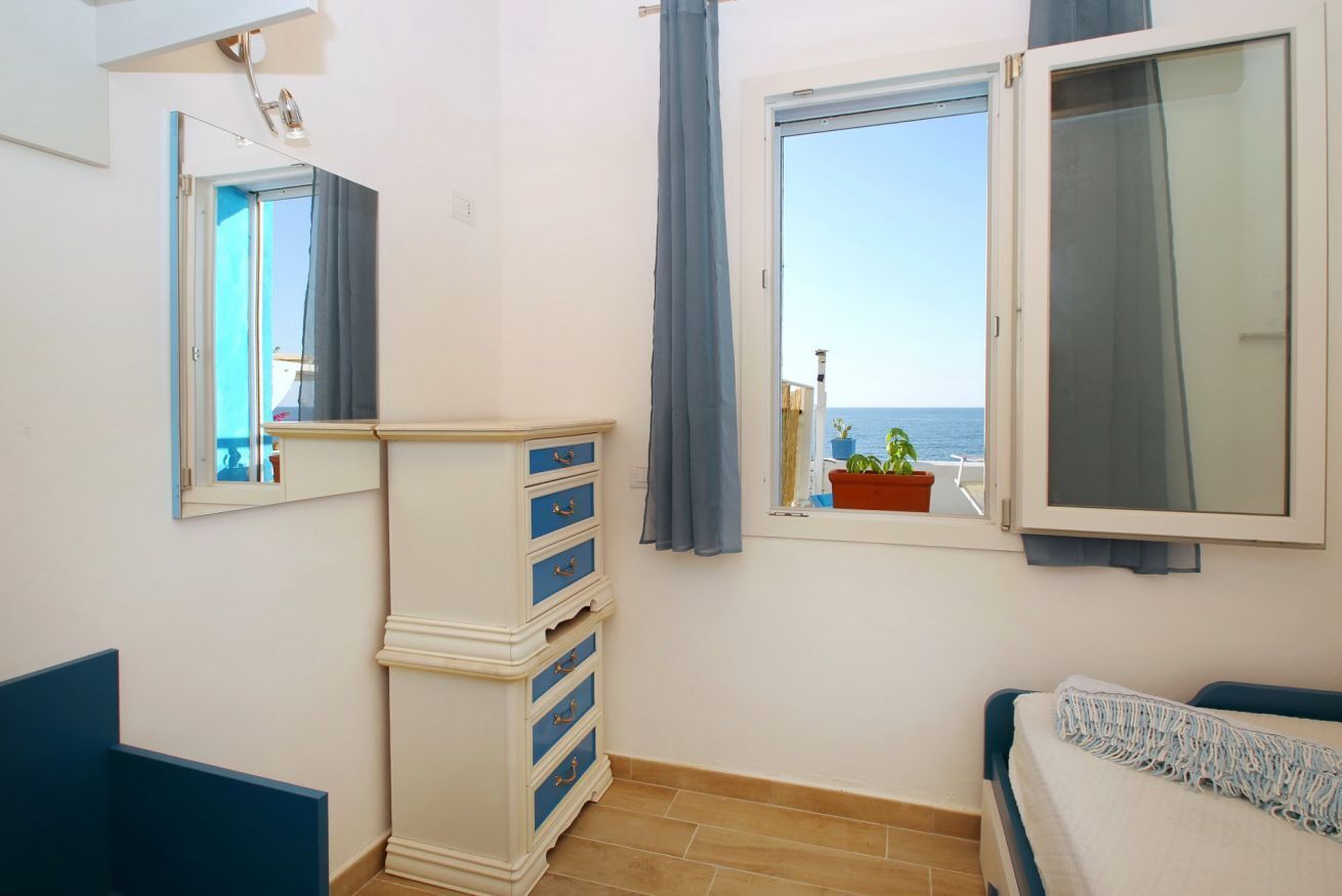 Un dormitorio con cama, cómoda, ventana con vista al mar y espejo en la pared.