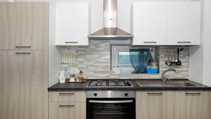 Une cuisine moderne avec des meubles en bois clair, des appareils électroménagers en acier inoxydable, un four encastré et une fenêtre offrant une belle vue.