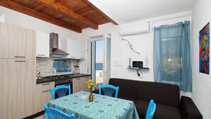 Een ruimtelijk ingerichte leefruimte met kitchenette, een eethoek met tafel en stoelen, een bank en uitzicht op de omgeving.