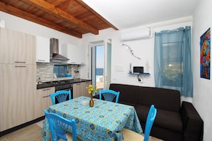 A compact living space with a kitchenette, a dining area with a table and chairs, a sofa, and a view of the outdoors.