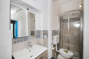 A bathroom with a white sink, a mirror, a toilet, and a glass-enclosed shower. - The Casello sul Mare is a historic railway house built in 1895 as a residence for railway workers and restored in 2025 while preserving its authentic charm. The property is set in a truly unique location, nestled between the railway and the sea, offering (Torremuzza)