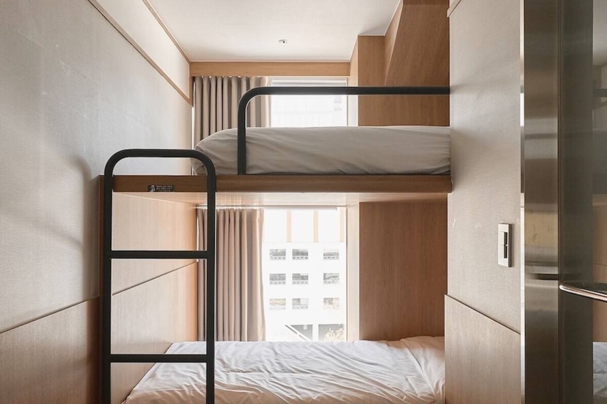 Een compacte hotelkamer met stapelbedden, een klein bureau en een kitchenette.
