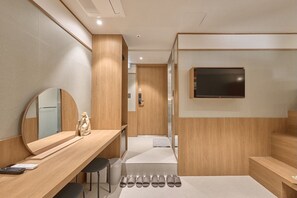 Habitació d'hotel moderna amb escriptori de fusta, un mirall gran, televisió penjada a la paret i prestatges per als sabatills.