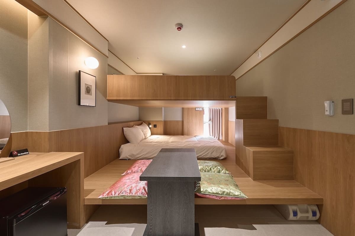 Een kleine kamer met een stapelbed, een bureau en een tafeltje.