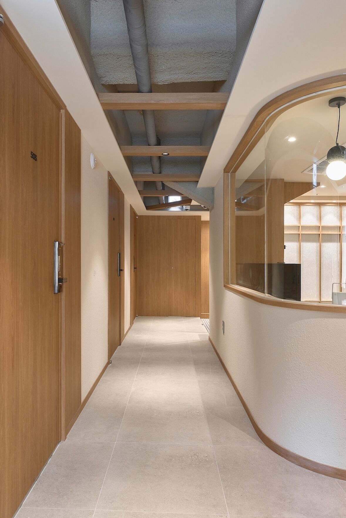 Un pasillo con puertas de madera, suelo de baldosas y una pared curva con un ventanal.