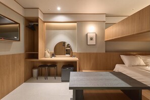 Habitació d'hotel compacta amb un llit, una taula de treball amb dues cadires, un petit rentapès i un mirall.