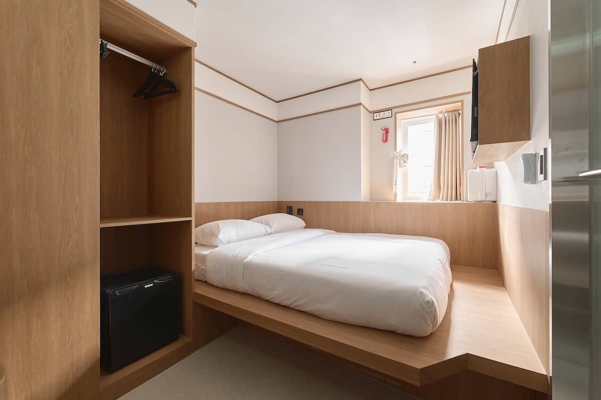 Een kleine hotelkamer met een bed, een kledingkast, een zithoekje en een koelkast.