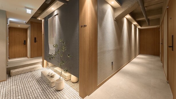 Een moderne hal met een structuurwand, een houten deur en een klein zithoekje met een plant.