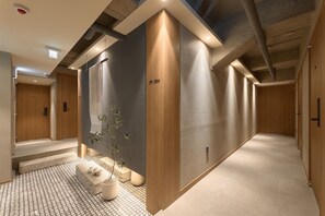 Un couloir moderne avec un mur texturé, une porte en bois et un petit coin salon agrémenté d’une plante.