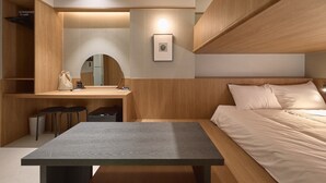 Een moderne slaapkamer met een houten hoofdbord, een nachtkastje, een bureau met stoel, een spiegel en een klein fotolijstje.